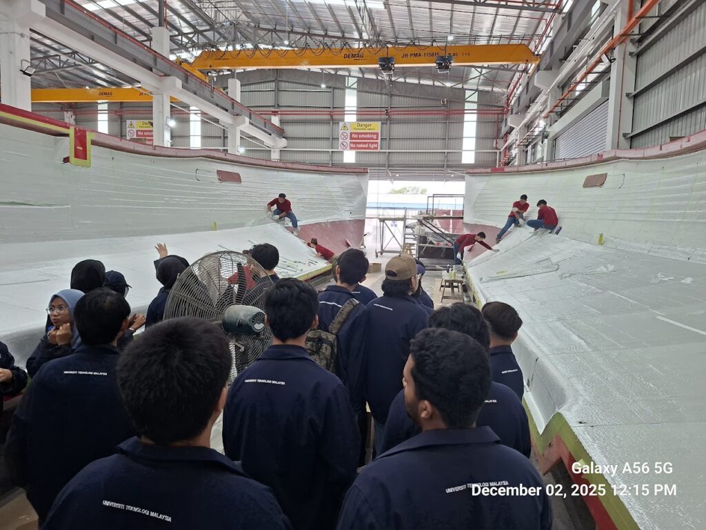 Students watching workers apply materials to the interior of a boat hull.